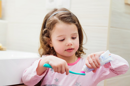 Little girl putting toothpaste on her toothbrush