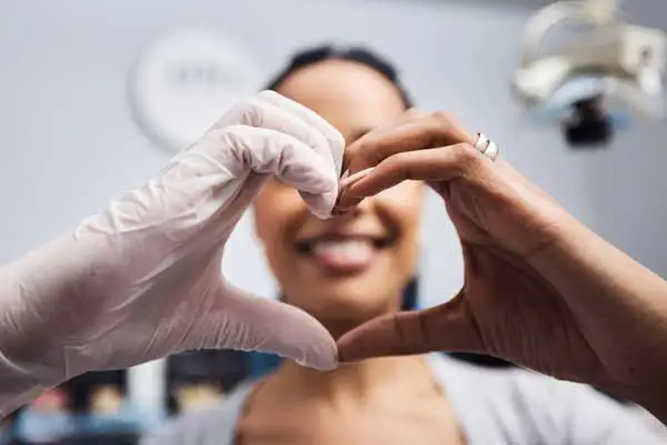 dental professional making a heart shape with her hands that frames her healthy smile in the background