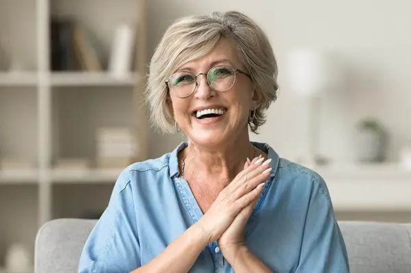 Cheerful pretty older woman in elegant glasses sitting on cozy home couchSinging River Dentistry in Madison, AL Cheerful pretty older woman in elegant glasses sitting on cozy home couchSinging River Dentistry in Madison, AL