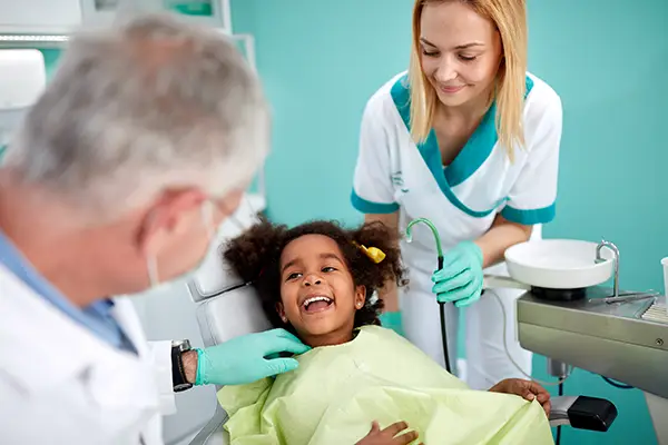 young patient sitting in a dental chair and smiling at her dentist and assistant