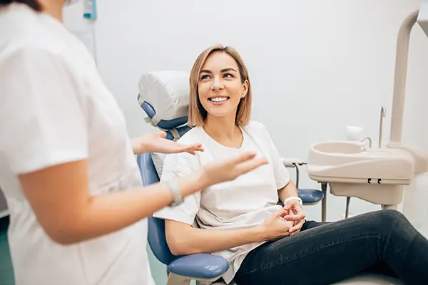 Smiling white patient calmly sitting a dental chair while her white dental assistant speaks with her