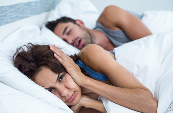 A Woman covering ears while husband with sleep apnea snores at Singing River Dentistry in Tuscumbia, AL