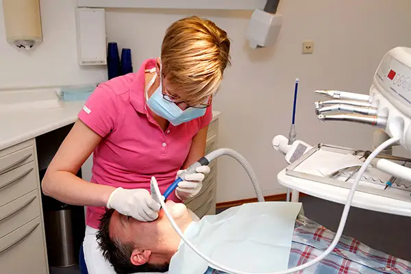 A dental hygienist thoroughly cleans a male patient's teeth while relaxes in his chair.