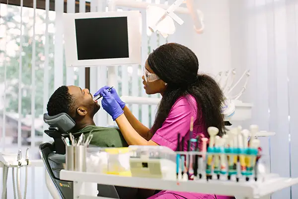 A dentist in a bright clinic examining a male patient's teeth, with dental instruments visible on the desk. A dentist in a bright clinic examining a male patient's teeth, with dental instruments visible on the desk.
