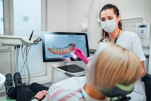 A dentist showing a 3D digital dental scan to a patient on a monitor during a consultation in a high-tech dental office.