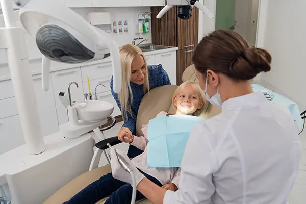 A dentist examining a young girl's teeth while her mother offers support in a modern dental clinic. A dentist examining a young girl's teeth while her mother offers support in a modern dental clinic.