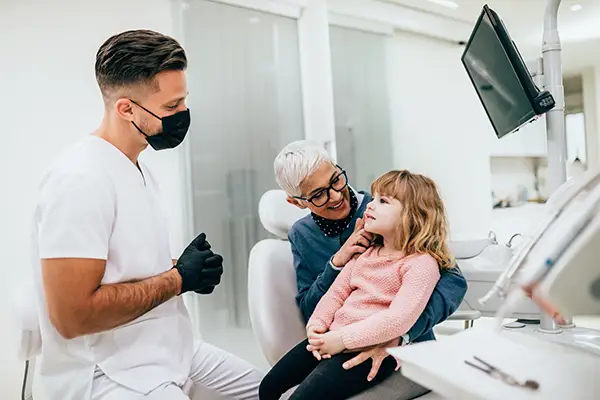 A cute little girl sitting in dentist chair before a routine dental procedure, accompanied by her grandmother. A cute little girl sitting in dentist chair before a routine dental procedure, accompanied by her grandmother.