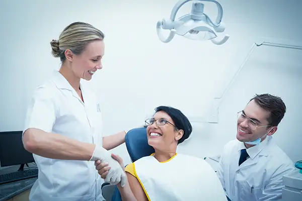 A woman smiling and shaking hands with her dentist and a dental hygienist to the side. A woman smiling and shaking hands with her dentist and a dental hygienist to the side.