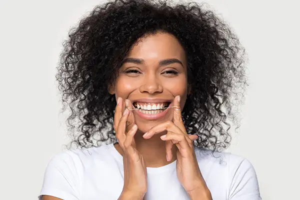 Smiling woman holding dental floss in her hands and demonstrating a proper flossing technique against a plain background. Smiling woman holding dental floss in her hands and demonstrating a proper flossing technique against a plain background.